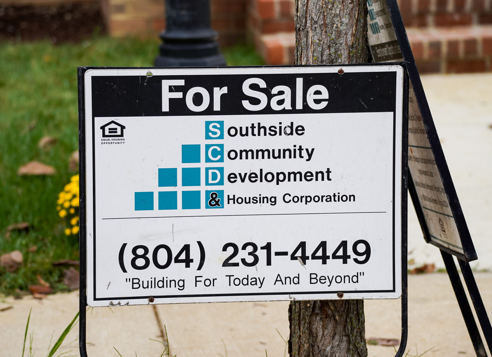 A For Sale sign for Southside Community Development & Housing Corporation, displaying their logo, phone number (804-231-4449), and the slogan Building For Today And Beyond, placed near a sidewalk and tree.