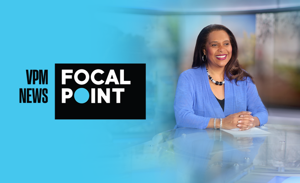 A smiling woman in a blue jacket sits at a news desk. To the left, there is a black and white VPM News Focal Point logo on a bright blue background.