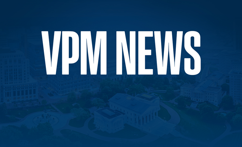 White text reading VPM NEWS in large, bold letters is displayed over a blue-tinted, aerial view of a city with buildings and greenery.